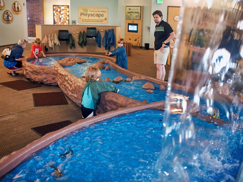 Grown-ups and children playing in water table inside the Playscape exhibit.